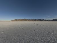 the bare desert has many footprints of people on it, with mountains in the background