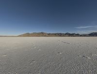 the bare desert has many footprints of people on it, with mountains in the background