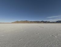 the bare desert has many footprints of people on it, with mountains in the background