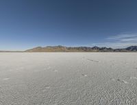 the bare desert has many footprints of people on it, with mountains in the background