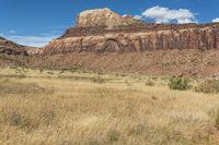 a red rock formation sitting high on top of a desert area with tall grass and tall trees