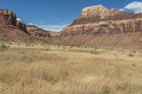 a red rock formation sitting high on top of a desert area with tall grass and tall trees