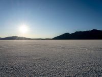 a desert with mountains and a lone skier during the sun set out in the distance