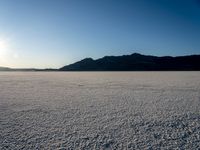 a desert with mountains and a lone skier during the sun set out in the distance