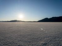 a desert with mountains and a lone skier during the sun set out in the distance