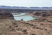 a desert area that has a river and a few hills in the background and a large body of water