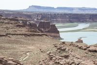 a desert area that has a river and a few hills in the background and a large body of water