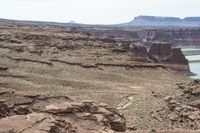 a desert area that has a river and a few hills in the background and a large body of water