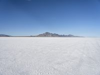 large expanse of white sand, with mountains in the distance in distance is blue sky