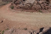 a person on a horse in the desert by some rocks and a steep hill behind it