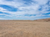 empty desert ground, in the middle of the day, with clouds overhead and blue skies above