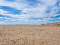 empty desert ground, in the middle of the day, with clouds overhead and blue skies above