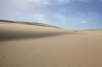 a lone person is walking in the middle of a desert with sand, one foot on the ground