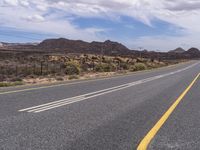 an empty road in the desert with yellow painted lines on it's sides and rocks with trees around it