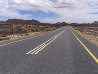 an empty road in the desert with yellow painted lines on it's sides and rocks with trees around it