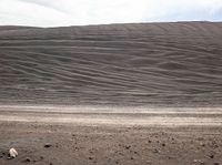 the desert has large mounds of rocks and gravel on the ground, one black horse in the foreground