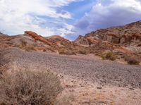 a desert with rocks and grass and shrubs under a cloudy sky over them is shown