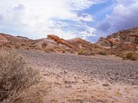 a desert with rocks and grass and shrubs under a cloudy sky over them is shown