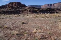 a desert with rocky terrain against a clear blue sky, in front of a big rock mountain