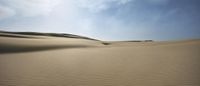 a lone sand dune in the desert under a partly cloudy sky, with no people standing and lying or sitting on it