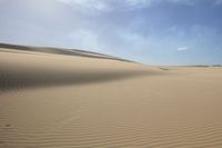 sand dune lines under a blue sky and clouds over a desert landscape with sparse, soft sands