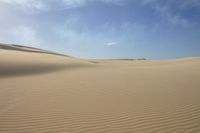 sand dune lines under a blue sky and clouds over a desert landscape with sparse, soft sands