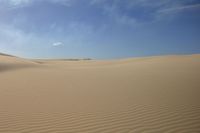 sand dune lines under a blue sky and clouds over a desert landscape with sparse, soft sands