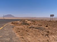 a road sign that points towards the distance on a desert road in an empty area