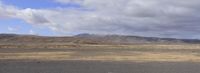 a lone vehicle traveling through the desert on a partly cloudy day, next to some mountains