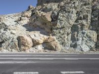 a motorcycle is traveling past a rock formation in the mountains along a road between two empty road divider