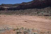 a large open barren area with rocks and scrub brush in the background and cliffs in the background