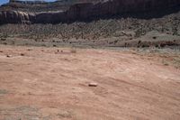 a large open barren area with rocks and scrub brush in the background and cliffs in the background