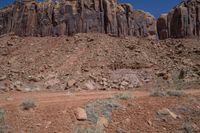 a dirt road through a desert plain with a mountain behind it and a clear blue sky in the background