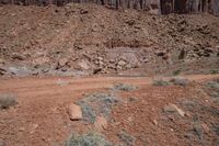 a dirt road through a desert plain with a mountain behind it and a clear blue sky in the background