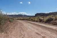 a dirt road on a sunny day with blue skies in the background / there is also a rock outcropping along the road