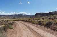 a dirt road on a sunny day with blue skies in the background / there is also a rock outcropping along the road