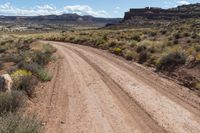 a dirt road on a sunny day with blue skies in the background / there is also a rock outcropping along the road