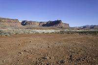 a desert area with a dirt ground and mountains in the distance with a blue sky in the background