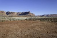 a desert area with a dirt ground and mountains in the distance with a blue sky in the background