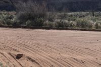 an empty dirt road in front of a mountain with a large brown piece of rock lying on the ground