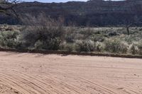 an empty dirt road in front of a mountain with a large brown piece of rock lying on the ground