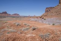 a dirt road through a desert plain with a mountain behind it and a clear blue sky in the background