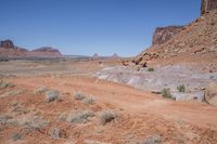 a dirt road through a desert plain with a mountain behind it and a clear blue sky in the background