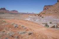 a dirt road through a desert plain with a mountain behind it and a clear blue sky in the background