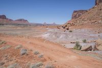 a dirt road through a desert plain with a mountain behind it and a clear blue sky in the background