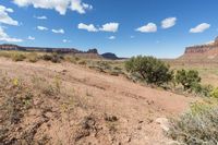 a very pretty view of some dirt mountains and trees in the background is blue and white clouds