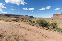 a very pretty view of some dirt mountains and trees in the background is blue and white clouds