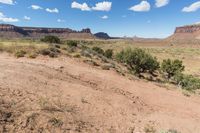 a very pretty view of some dirt mountains and trees in the background is blue and white clouds