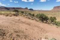 a very pretty view of some dirt mountains and trees in the background is blue and white clouds