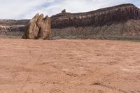 an odd rock on a desert area with mountains in the background, with white clouds